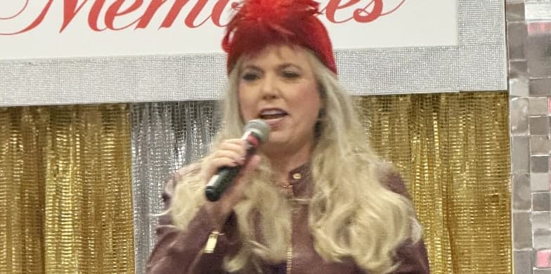 Michelle Lee in a red feathered hat, holding a microphone in front of a gold curtain