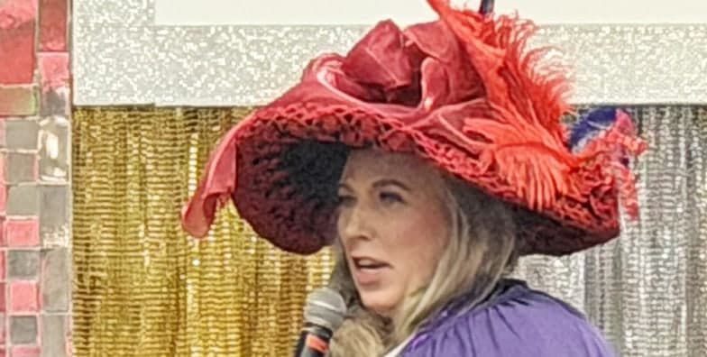Michelle Lee in a wide red feathered hat, speaking into a microphone