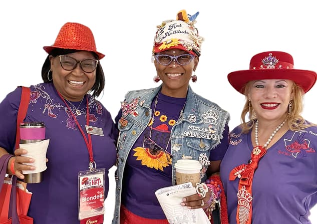 Three smiling members in red hats and purple outfits at a Red Hat Society gathering