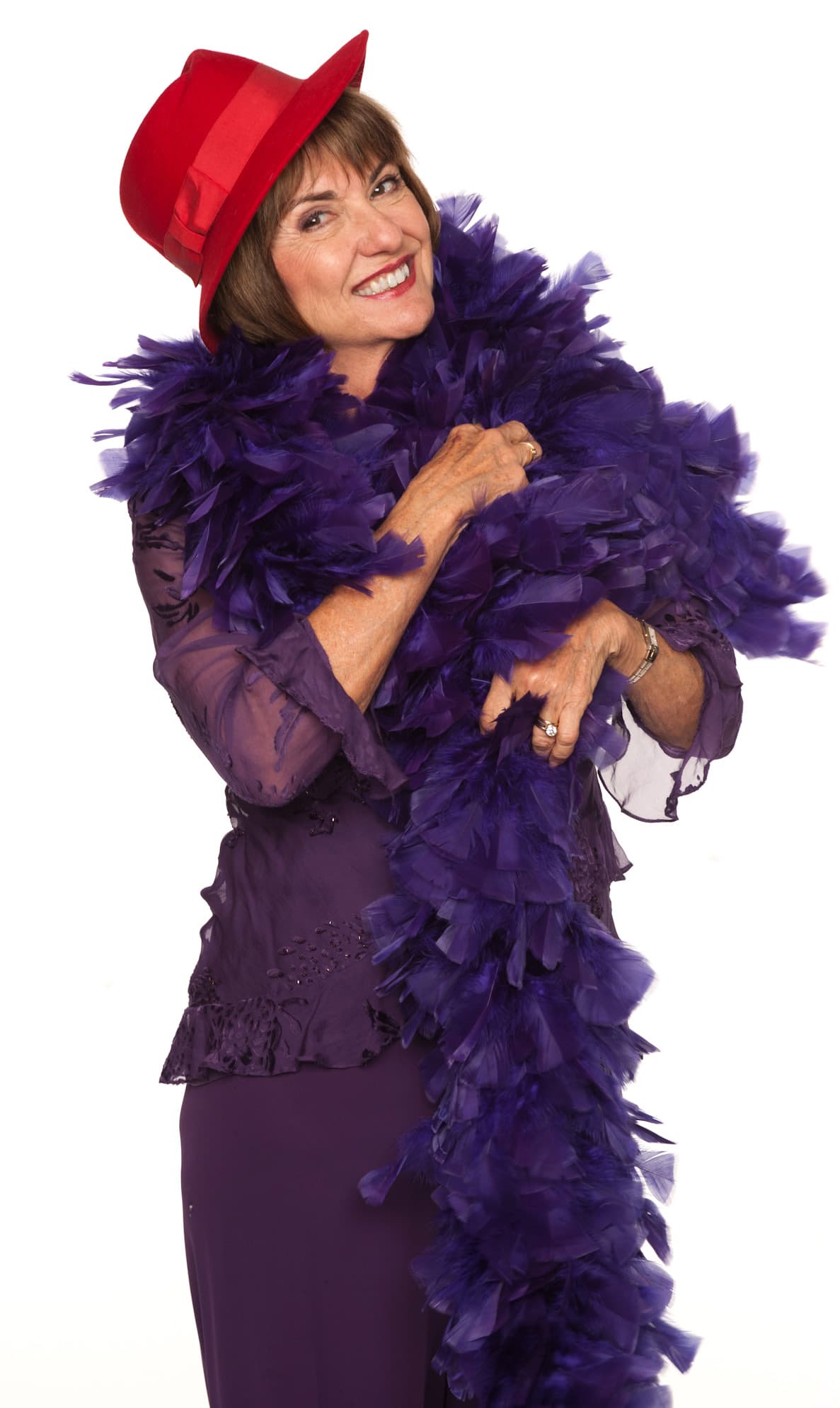 Sue Ellen Cooper smiling in a red hat and purple outfit, wrapped in a purple feather boa.
